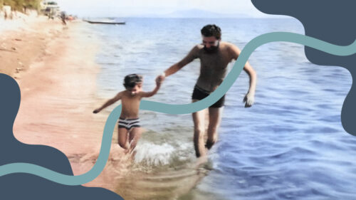 Retro film photo of a father and a young son holding hands and running in the water at a beach.