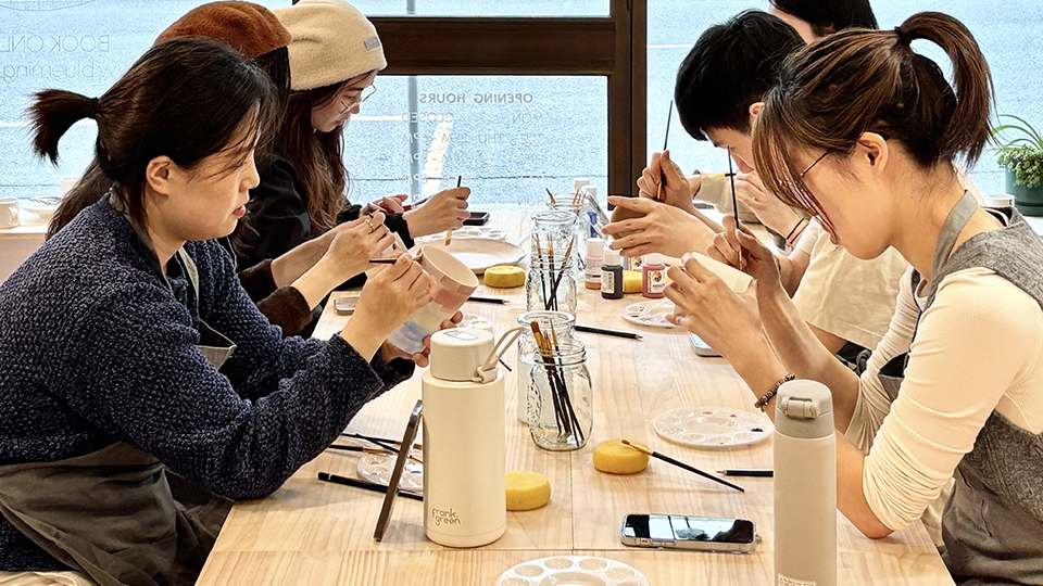 Image of a group of people painting handcrafted mugs in a pottery and painting workshop at Blueming Pottery