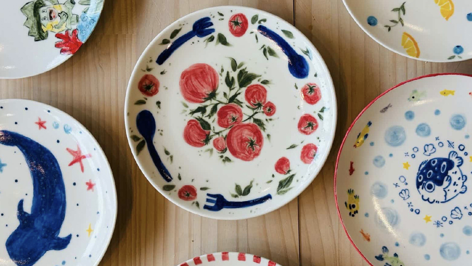 Close up photo of a finished ceramic plate that has been painted with images of tomatoes and flowers.