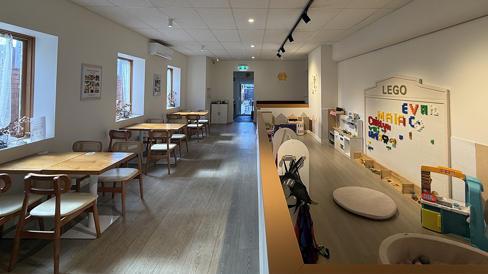 Indoor photo of Minori Cafe in Camberwell Junction, with neat rows of clean dining tables to the left, and an enclosed play area filled with toys and legos on the wall to the right of the image.